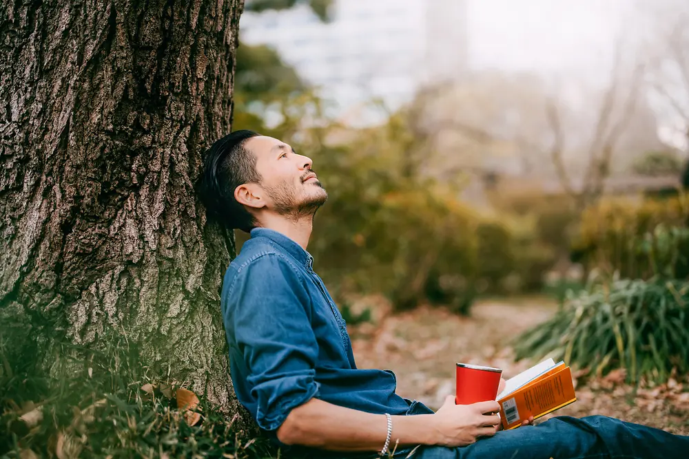 Seorang pria dengan buku bersandar di pohon